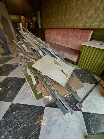 Interior remodel debris and broken drywall piled on a checkered tile floor before junk removal